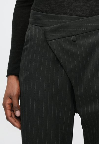 Crne hlače s prugicama s jedinstvenim omotanim dizajnom u struku. Tekstura tkanine čini se glatkom i lagano sjajnom, što pruža moderan siluetu.
