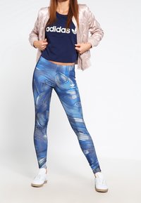 Modré legíny s vířivými vzory, spárované s námořnickou tričkem s bílým logem a světle růžovou vypolstrovanou bomber bundou. Bílé sneakers.