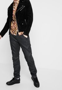 Chaqueta de moto de ante negra con cremalleras plateadas, camisa de flores estampada, pantalones de cuero negros y zapatillas negras con cordones.
