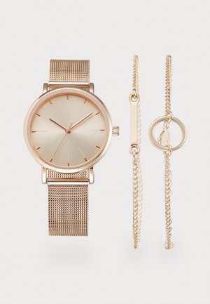 Montre à bracelet en maille or rose avec un cadran rond uni et deux bracelets chaînes délicats assortis, l'un avec une barre et l'autre avec un fermoir circulaire.