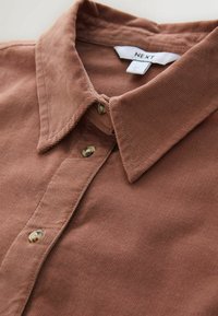 Brown corduroy shirt with a pointed collar, featuring round buttons and a subtle ribbed texture, label visible at the neckline.