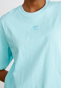 Ljusblå bomullströja med rund halsringning och korta ärmar. Litet vitt broderat Adidas-logotyp på bröstet.