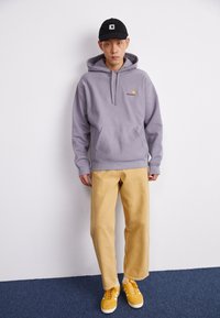 Gray hooded sweatshirt with a front pocket, paired with beige wide-leg pants and yellow suede sneakers. Black cap with logo accents.