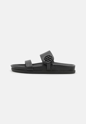 Schwarze Slidesandale mit zwei Riemen, der vordere Riemen ist schlicht, der obere Riemen mit einem runden Logodetail versehen.
