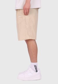Shorts écossais beiges avec une texture subtile, poches latérales et un patch logo. Associés à des baskets blanches et des chaussettes avec un logo.