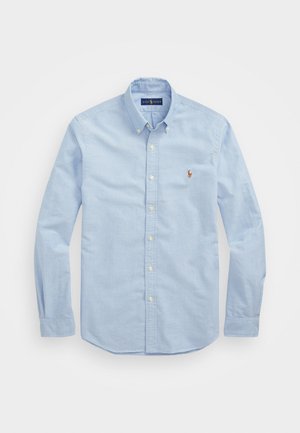 Camisa de botão de manga longa azul-claro, feita de algodão, com um colarinho clássico e um pequeno logótipo bordado em vermelho no peito.