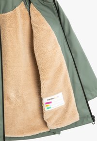 Grön ytterjacka med en mjuk beige fleece-foder. Har en dragkedjestängning och en tygetikett med skötselinstruktioner.