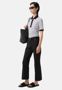 Polo rayé noir et blanc, ceinture noire, pantalon large noir, sandales noires et sac fourre-tout en noir texturé.