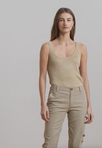 Šviesiai beige juostelėmis marškinėliai su plačiomis petnešomis, derinami su šviesiai rudo atspalvio kelnėmis, turinčiomis mygtuko užsegimą ir �šonines kišenes.