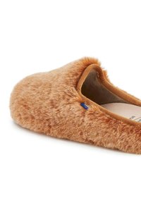 Bruine fuzzy pantoffel met een zachte, gestructureerde buitenkant en een ronde neus. Beschikt over een pluche voering en een blauwe logo-accent aan de zijkant.