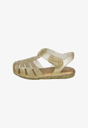 Sandalias doradas brillantes con diseño abierto, cinta alrededor del tobillo y recortes decorativos. Suela texturizada y marca en el lateral.
