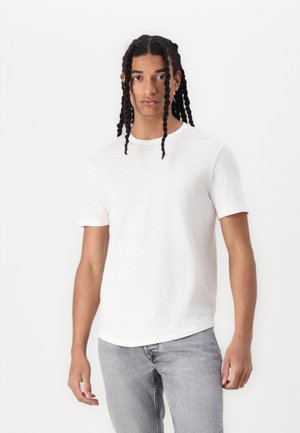 White short-sleeve T-shirt with a round neckline, made of a lightweight material, worn with gray jeans. Simple design with a textured finish.