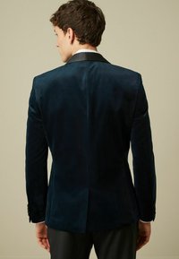 Blazer in velluto blu navy con rever in satin, maniche lunghe e spacco singolo sul retro. Vestibilità sartoriale con dettagli a bottoni sulle maniche.