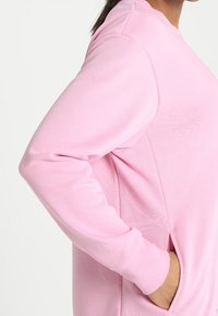 Sudadera rosa claro con un diseño sencillo, que cuenta con mangas largas y bolsillos laterales, confeccionada con una tela suave y texturizada.