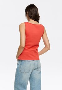Top rosso senza maniche con scollatura rotonda e design aderente, abbinato a jeans di denim chiaro a vita alta. Texture liscia, look casual.