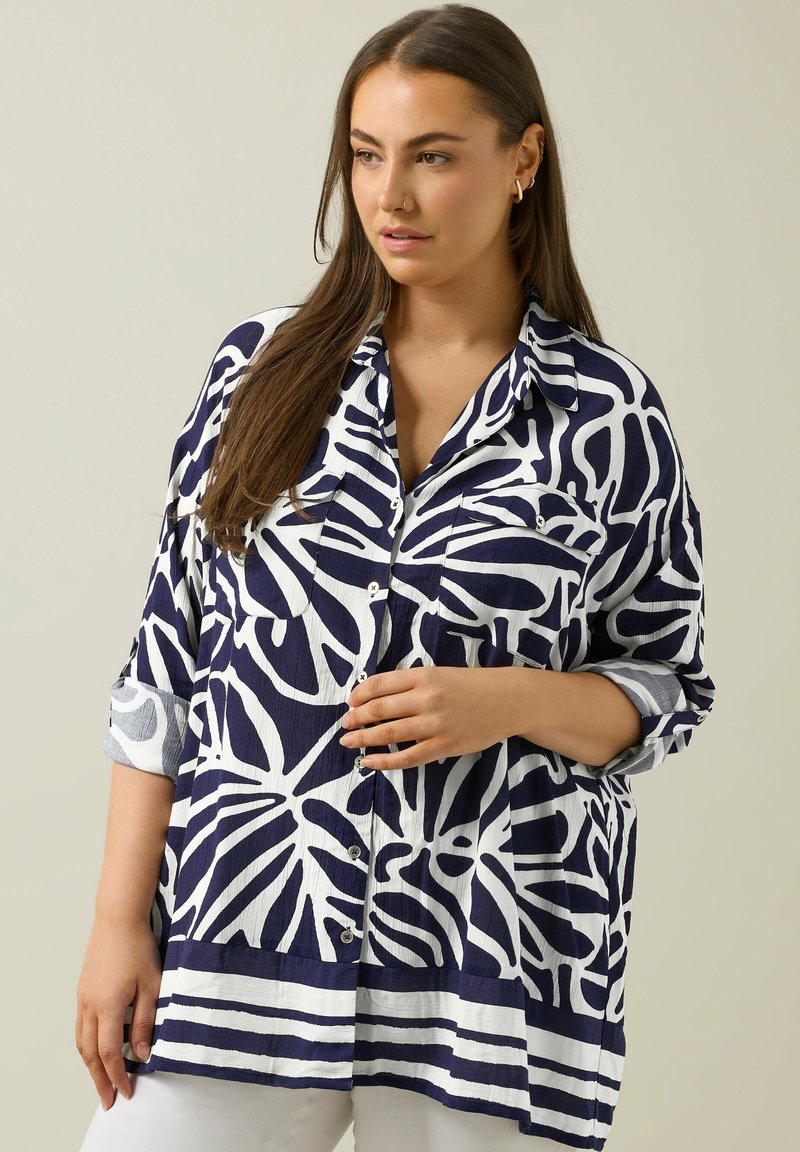 Marineblauwe en witte oversized blouse met bladerenpatroon, knoopsluiting aan de voorkant, opgerolde mouwen en een gestreepte zoom, gemaakt van lichtgewicht stof.