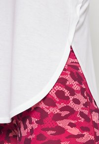 Top bianco a maniche corte con orlo curvo abbinato a leggings con stampa animale rosa e rossa caratterizzati da texture sovrapposte e colori in contrasto.