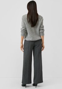 Grauer, gerippter Pullover mit langen Ärmeln, kombiniert mit dunkelgrauer, weit geschnittener Hose. Glatte Textur und taillierte Passform betonen die Silhouette.