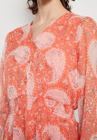 Rot-orange Kleid mit floralem Paisleymuster, V-Ausschnitt, elastischem Bund und durchsichtigen langen Ärmeln. Weicher, leichter Stoff.