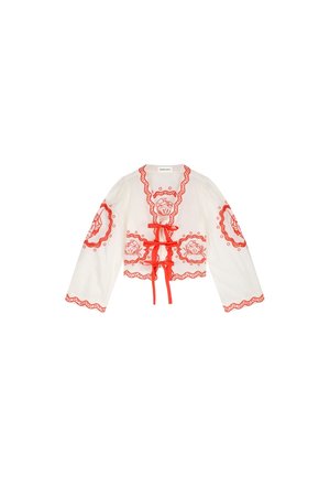Witte cropped top met lange mouwen, voorzien van rode bloemige borduursels, rode gegolfde randen en drie rode striksluitingen aan de voorkant.
