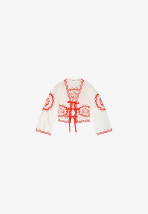 Witte cropped top met lange mouwen, voorzien van rode bloemige borduursels, rode gegolfde randen en drie rode striksluitingen aan de voorkant.