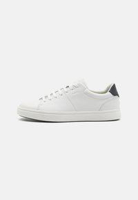 Baskets blanches en cuir texturé avec une semelle blanche, présentant des accents gris au niveau du talon et cinq paires d'œillets en métal pour les lacets.