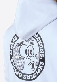 Felpa bianca con un grande grafico nero della faccia di un personaggio dei cartoni animati, con motivi a pois e il testo "DOVE SI RACCOLGONO I CATTURATORI."