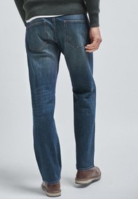 Jeans in denim blu scuro con taglio a gamba dritta, dotati di due tasche posteriori e una leggera sfumatura. Indossati con stivali marroni.