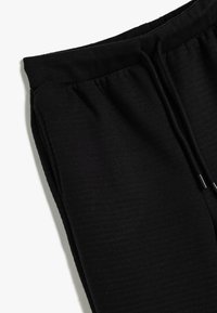 Pantalones de chándal negros con una cinturilla acanalada y cordón ajustable. Textura suave con un acabado liso y sin patrones ni acentos visibles.