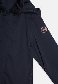 Navy blue outerwear with a soft texture, featuring a hood, shoulder seams, and a round logo patch on the left arm.