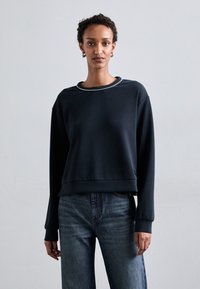Sudadera navy con cuello redondo, corte relajado y puños de canalé. Combinada con unos vaqueros de color azul claro, que presentan una tela de denim texturada.