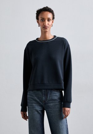 Navy sweatshirt with a round neck, relaxed fit, and ribbed cuffs. Paired with light blue jeans, featuring a textured denim fabric.