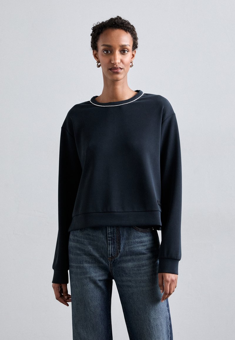 Sudadera navy con cuello redondo, corte relajado y puños de canalé. Combinada con unos vaqueros de color azul claro, que presentan una tela de denim texturada.