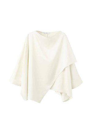 Asymetrický slonovinový top ve stylu ponča se širokými rukávy a vrstveným přehozem na jednobarevném pozadí.