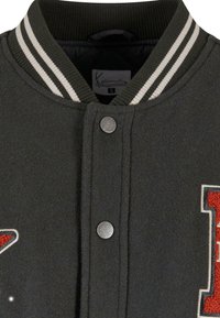 Grå ull varsity-jakke med ribbet svart krage, sølvfargede trykknapper og røde broderte detaljer med hvite konturer.