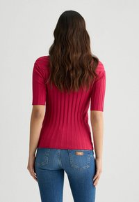Top scurt cu mânecă scurtă, ribbed, într-o nuanță vibrantă de roz, cu un design ajustat, material texturat și un finisaj neted. Asortat cu blugi albaștri.
