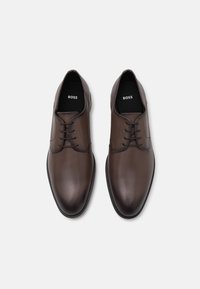 Scarpe eleganti in pelle marrone con una finitura liscia, punta tonda e allacciatura a cinque fori. Presentano un logo discreto sulla soletta e una suola testurizzata.