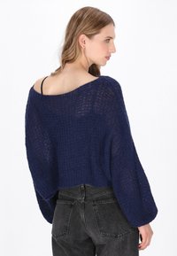 Granatowy sweter z dzianiny o luźnym kroju, szerokich rękawach i designie bez ramiączek. Teksturowany materiał, krótka długość, w połączeniu z szarymi dżinsami.