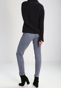 Suéter de punto negro con cuello alto, combinado con jeans ajustados de lavado medio y botas negras hasta el tobillo. Conjunto casual de textura fina.