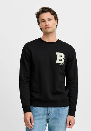 Sudadera negra de algodón, con cuello redondo y puños de canalé, que presenta un parche beige con la letra "B" en la parte izquierda del pecho.