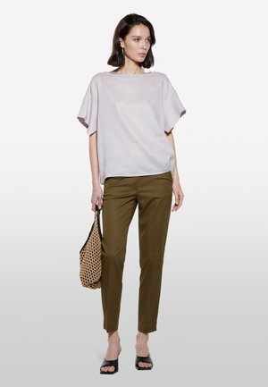 Top grigio chiaro, dalla vestibilità ampia con maniche larghe, abbinato a pantaloni verde oliva a gamba affusolata. La modella porta una borsa intrecciata e indossa sandali neri a ciabatta.