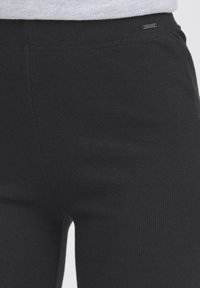 Zwarte geribbelde stoffen broek met een elastische tailleband en minimale detailing. Bevat een klein merketiket dat op de taille is gestikt.