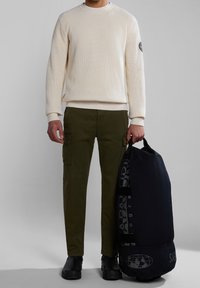 Světle krémový svetr s ribováním, olivové cargo kalhoty a černá taška přes rameno s šedým logem. Hladký povrch a funkční kapsy jsou viditelné.