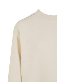 Pull beige à col rond montrant un col côtelé et un tissu tricoté lisse sur l'épaule et le haut de la manche.