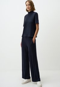 Marineblauw tweedelig outfit met een top met korte mouwen en een hoge kraag, en een broek met wijde pijpen, gemaakt van gestructureerde stof, met zijzakken.