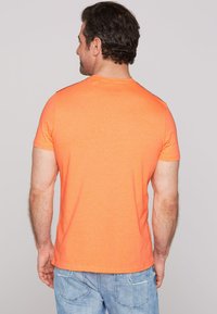 Tílko s krátkým rukávem a kulatým výstřihem v jasně oranžové barvě. Má hladkou texturu a jednoduchý design bez vzorů nebo akcentů.