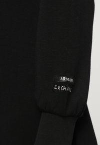Manche noire avec poignet élastique présentant un texte blanc brodé "EXCHANGE" et une petite étiquette noire avec texte blanc "ARMANI".