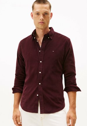 Bordeaux knoopshirt gemaakt van gestructureerde stof, met een knoopkraag en opgerolde mouwen. Klein logo bij de borst, witte knopen.