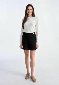 Biała bluzka z długim rękawem i okrągłym dekoltem, ozdobiona akcentami na ramionach, zestawiona z czarnymi szortami o wysokim stanie z boczną klamrą.