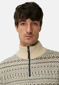 Gebreid pullover in crème en grijs met geometrische patronen, voorzien van een hoge ribgebreide kraag en een zwarte rits aan de voorkant.